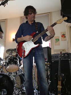 Foto van Jos Oerlemans met gitaar voor een drumstel en geluidsapparatuur