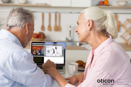 Man en vrouw voor laptop met online presentatie Oticon Medical